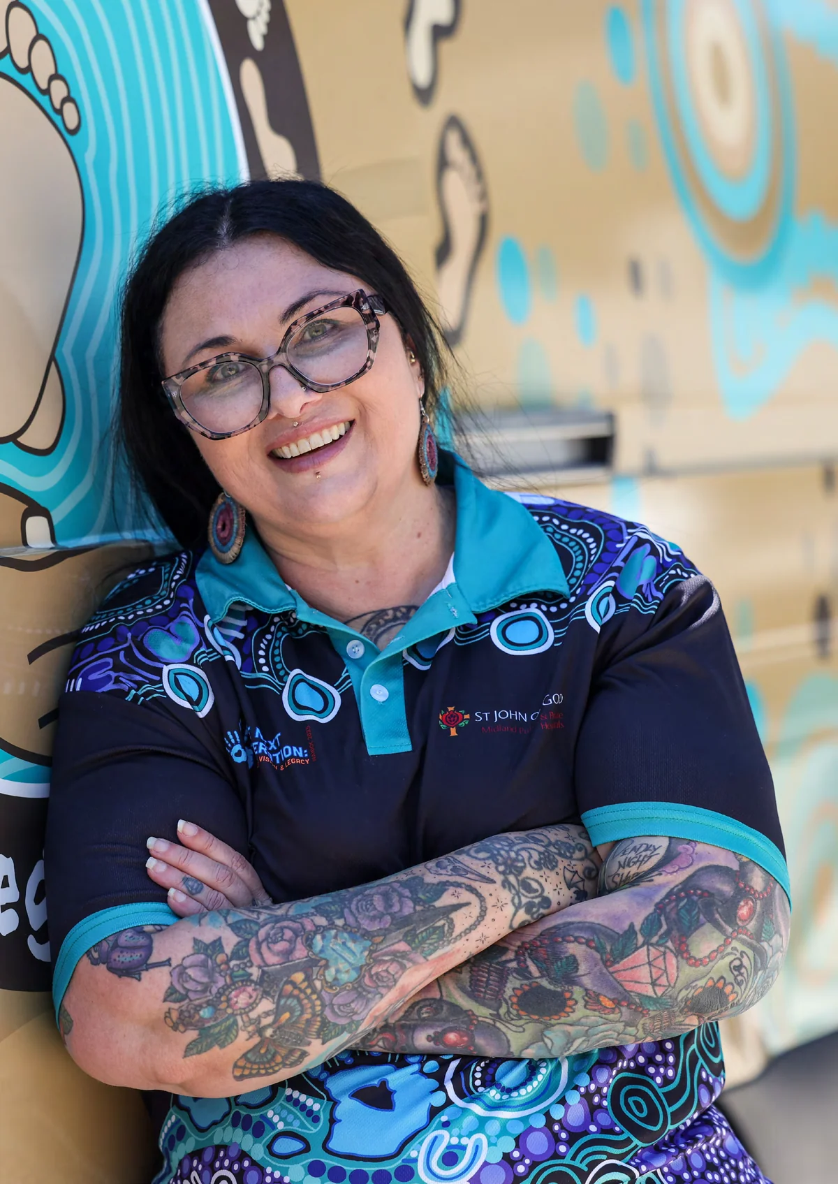 Midwife Jodee Hollingsworth leaning against a vehicle painted with Aboriginal artwork
