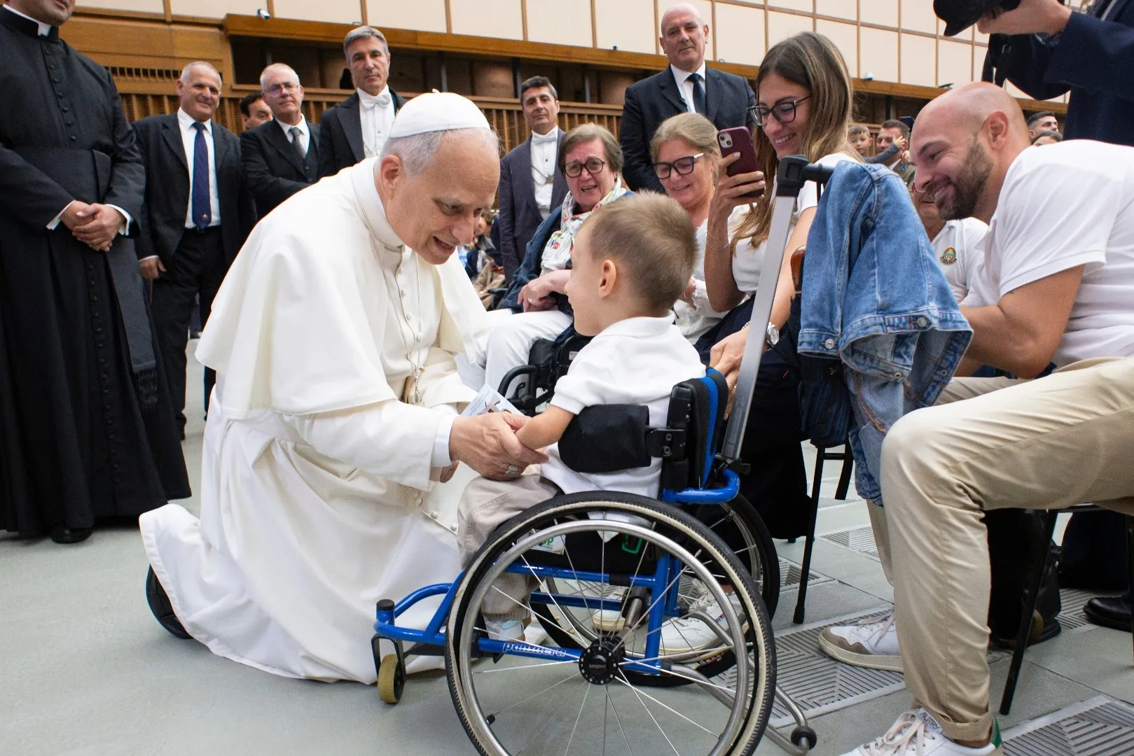 Pope Leo XIV holding the hands of a child seated in a wheelchair